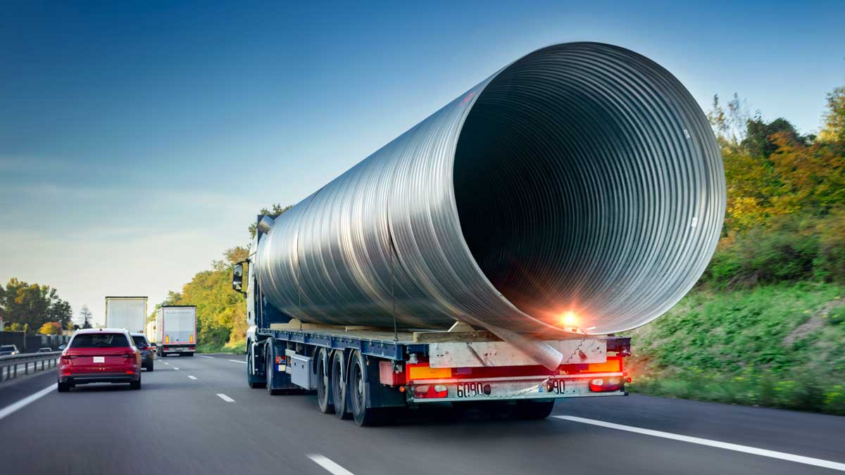 truck driver with large metal pipe drives down highway